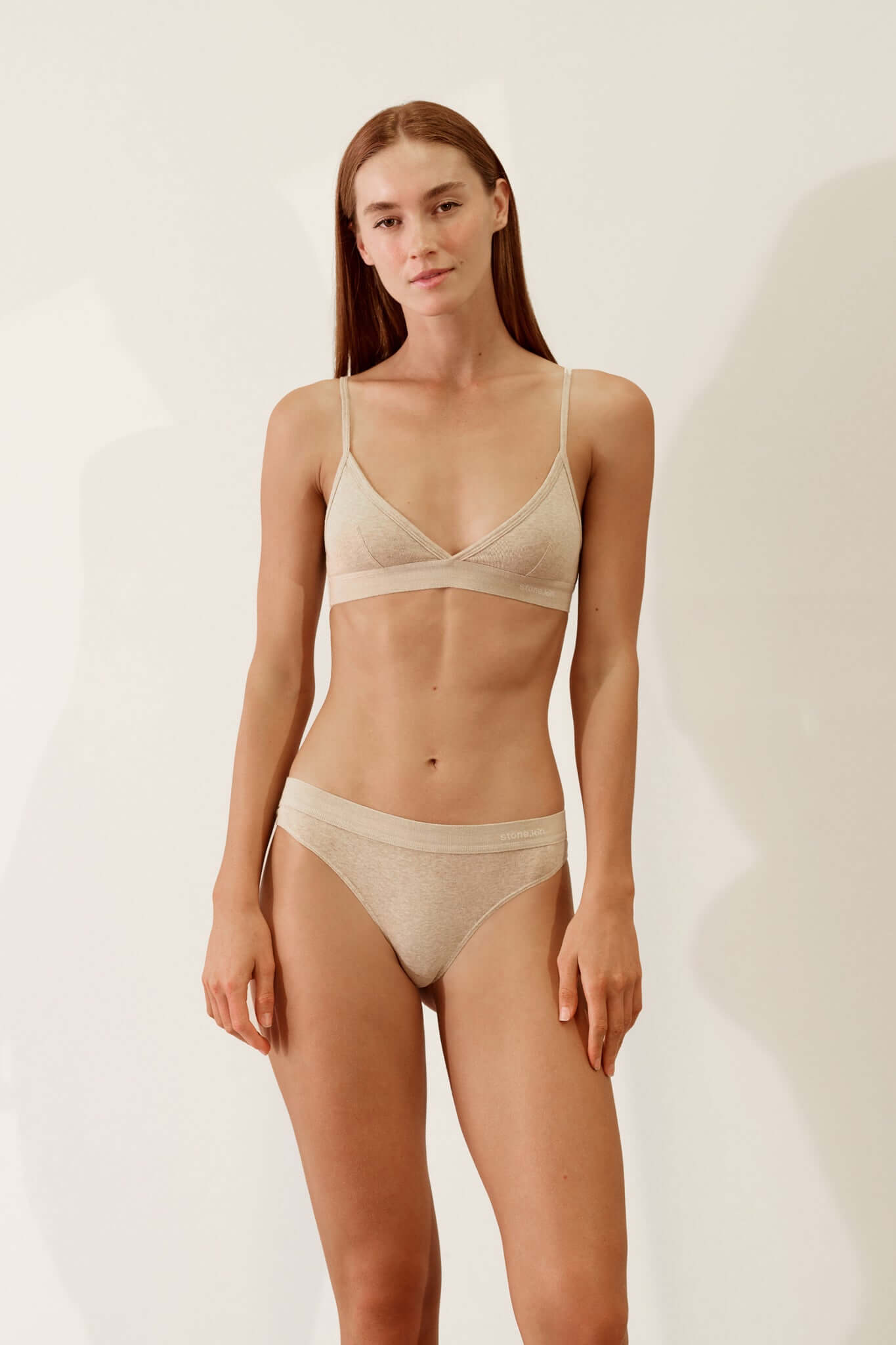 Thong in Organic Cotton Rib - Sand modeled by a woman, showcasing its soft, breathable design in a minimalist setting.