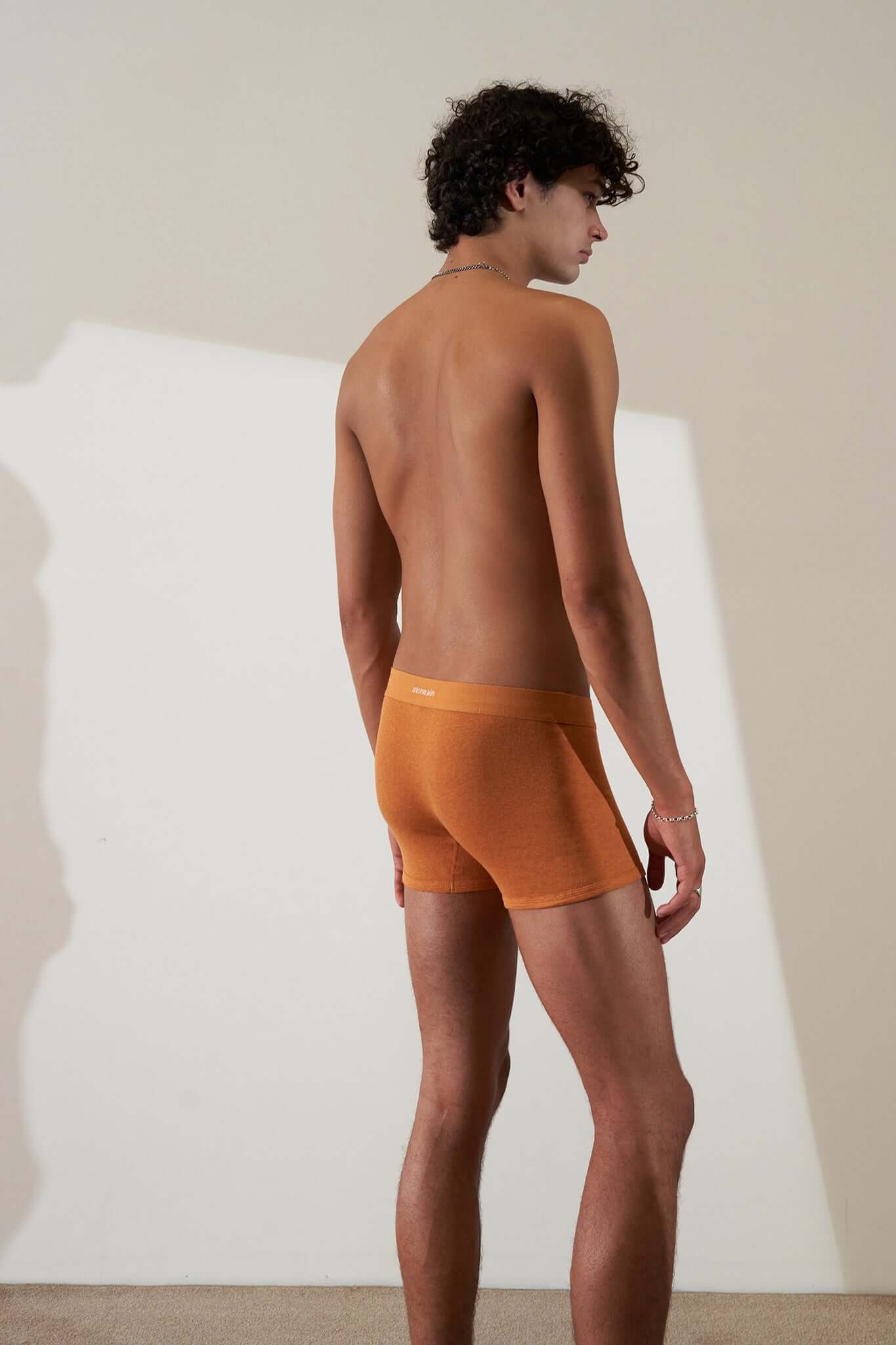 Model wearing the Boxer Brief 3 Pack in Organic Cotton, showcasing the Papaya colored boxer briefs from the back.